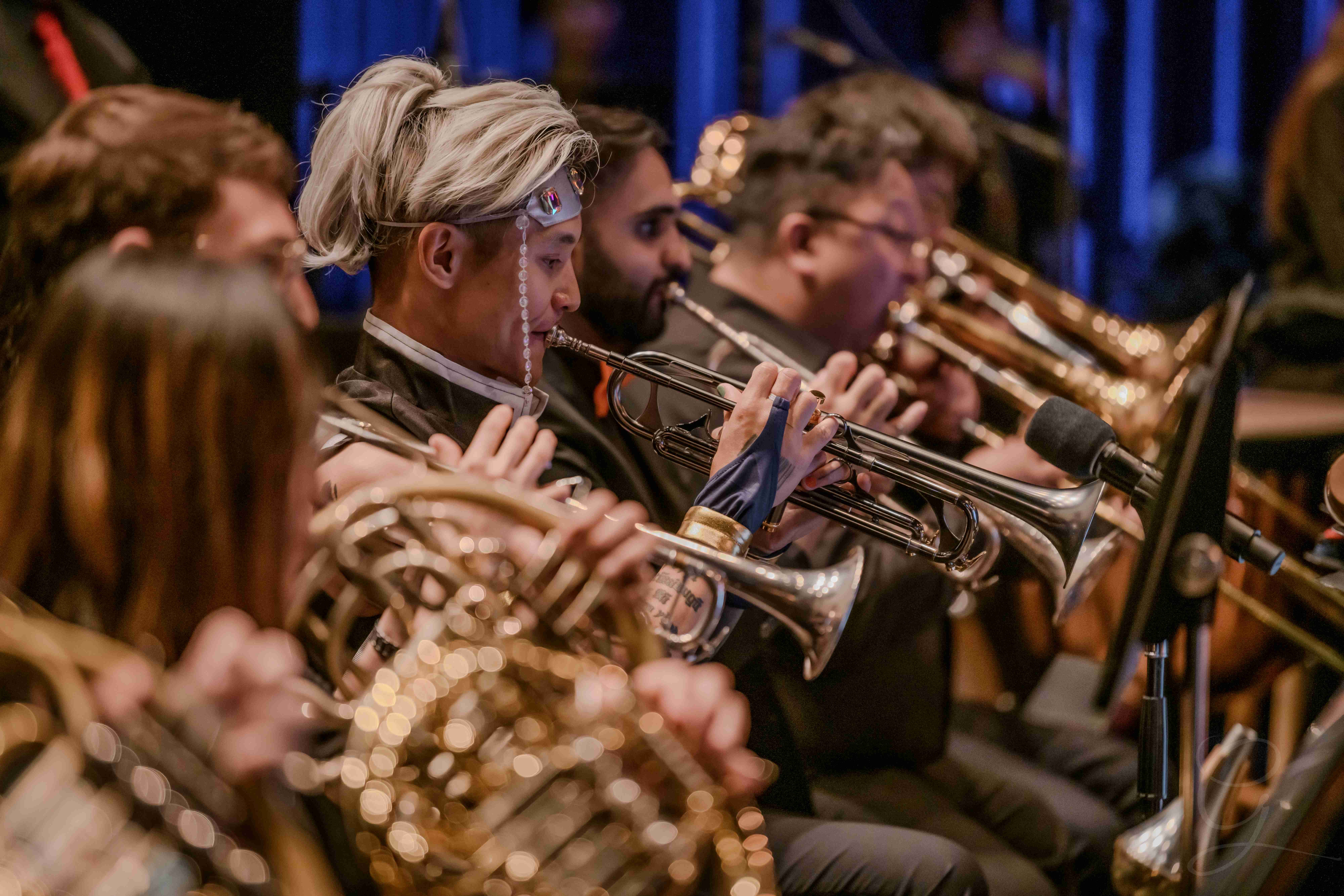Costumed trumpet player performing with the brass section under blue stage lighting